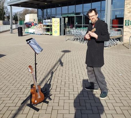 Picture of Eric performing in Bolsover, outside supermarket, stand and additional uke visible.