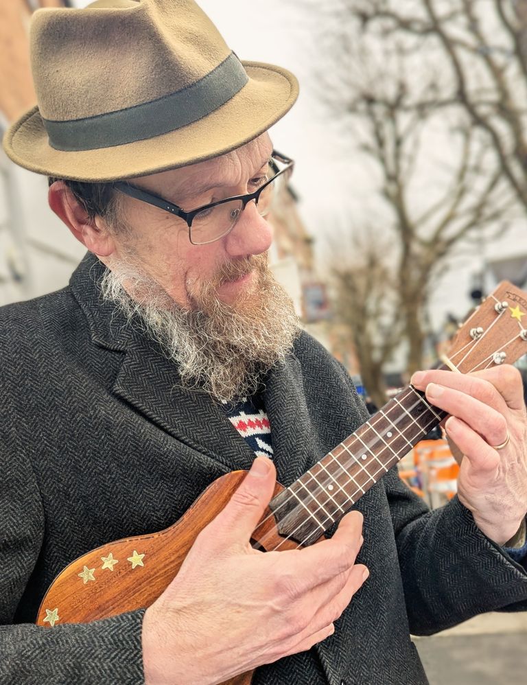 Eric (in a hat) playing his concert uke, outside.