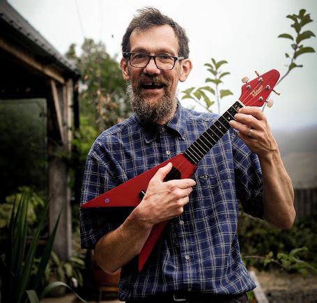 Outside photo of Eric posing with Red flying-v uke.