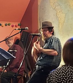Eric in mid-flow, playing uke at a microphone, indoor setting.